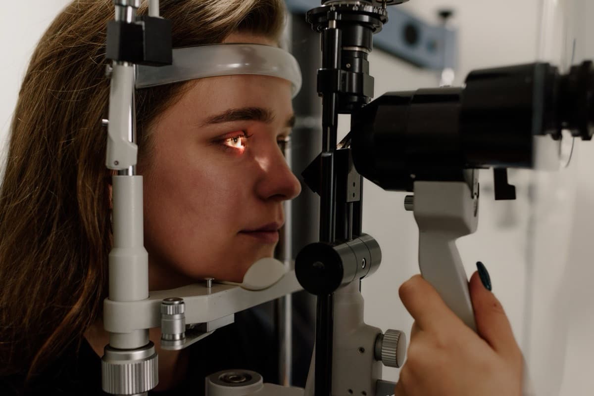 Pacijentkinja naslonjena bradom na biomikroskop dok joj lekar snopom svetlosti pregleda oko